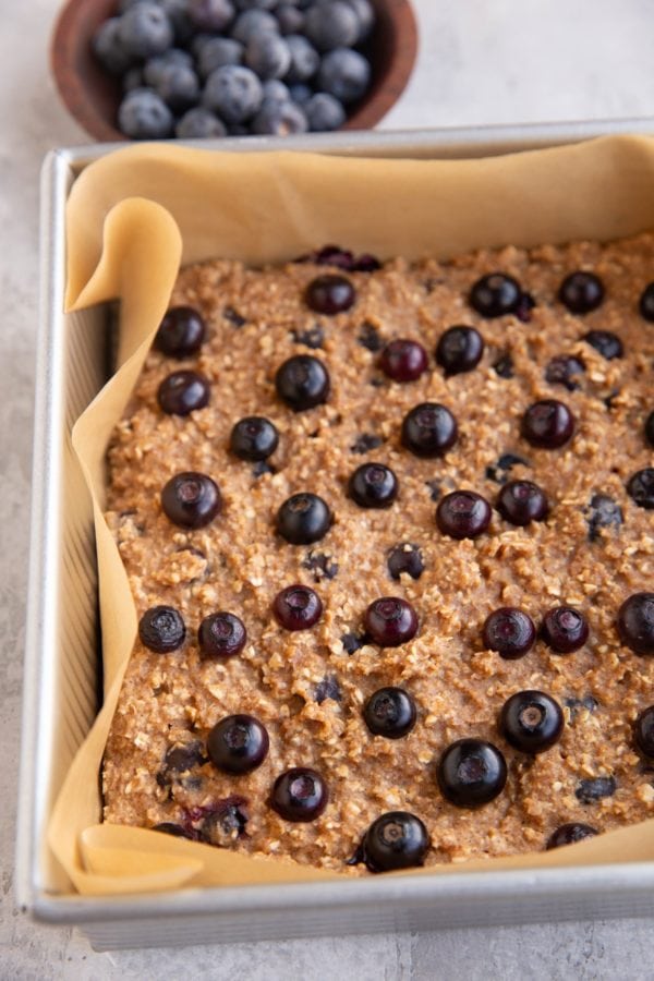 Baking dish with blueberry oatmeal bars fresh out of the oven and a bowl of fresh blueberries in the background.