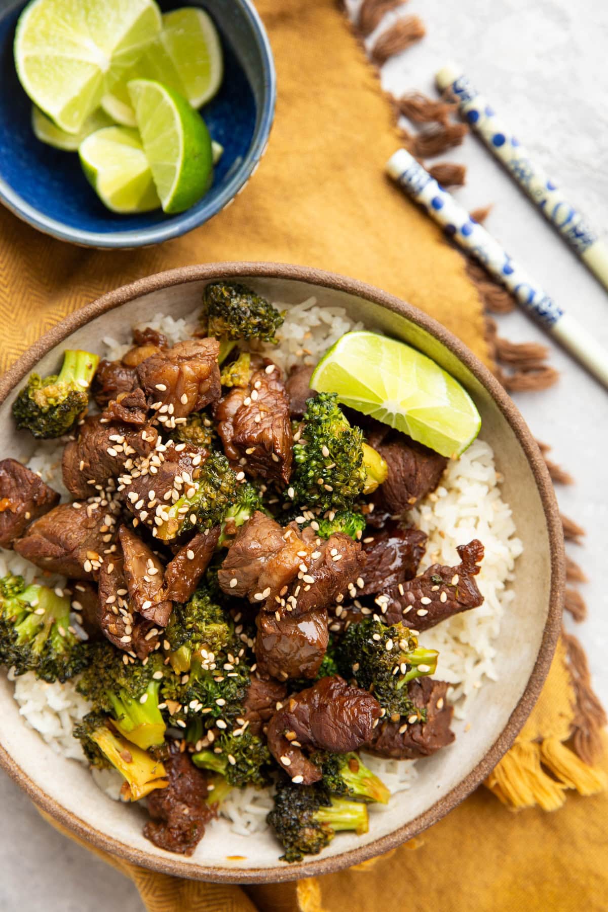 Broccoli beef in a bowl with rice and a lime wedge. Chopsticks to the side and fresh lime wedges.