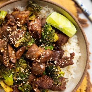 Bowl full of chopped beef, broccoli florets, and rice. Chopsticks and fresh limes to the side.