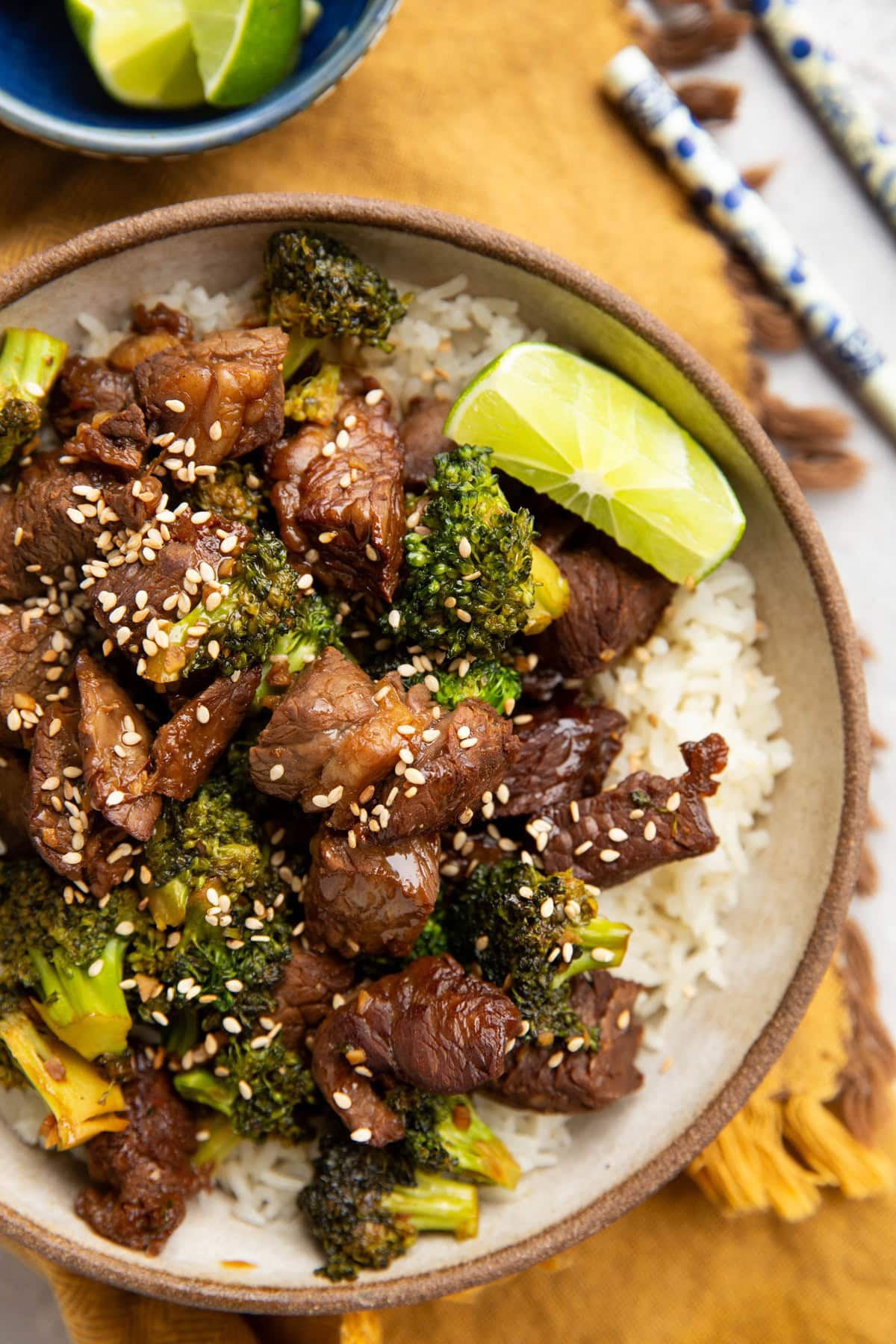 Bowl full of chopped beef, broccoli florets, and rice. Chopsticks and fresh limes to the side.