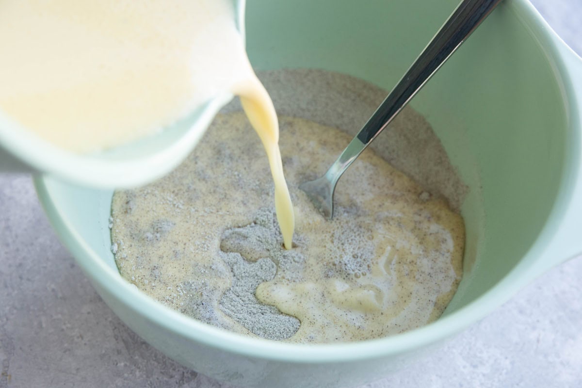 Mixing bowl with flour inside and wet ingredients being poured in.