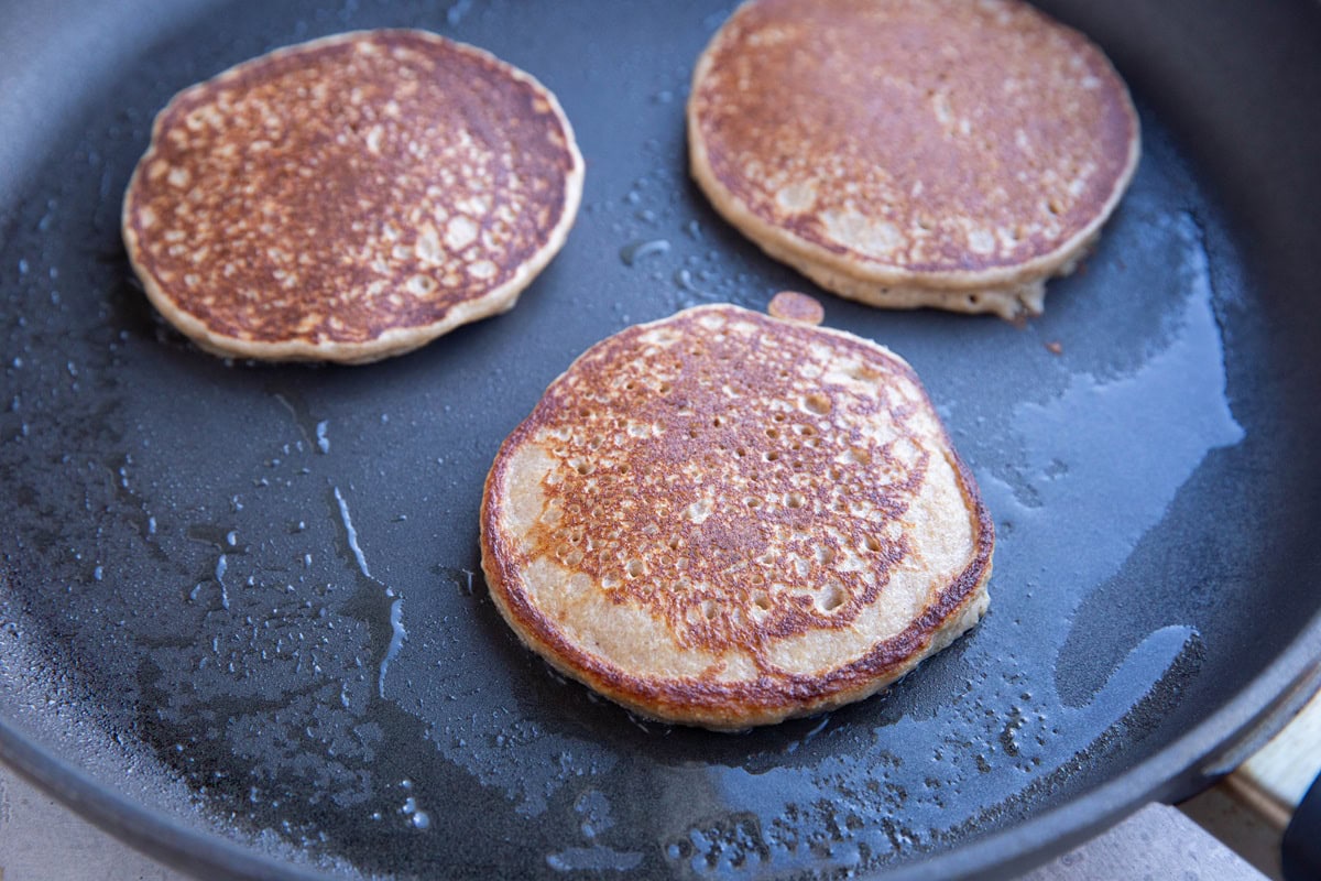 Hot skillet with three pancakes cooking. Golden brown and delicious looking.