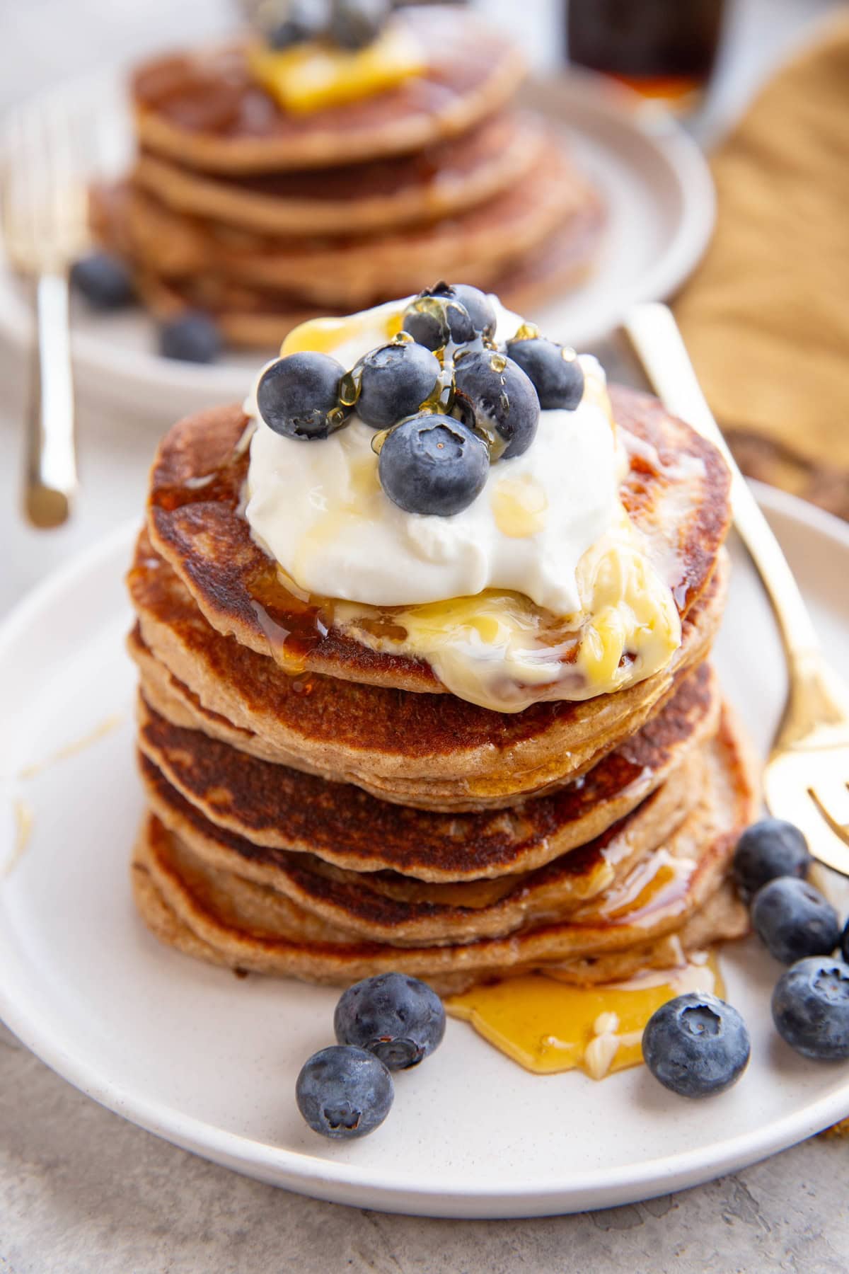 Stack of pancakes with yogurt, berries, butter, and honey on top.