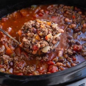 Crock pot full of chili with a ladle scooping some out.