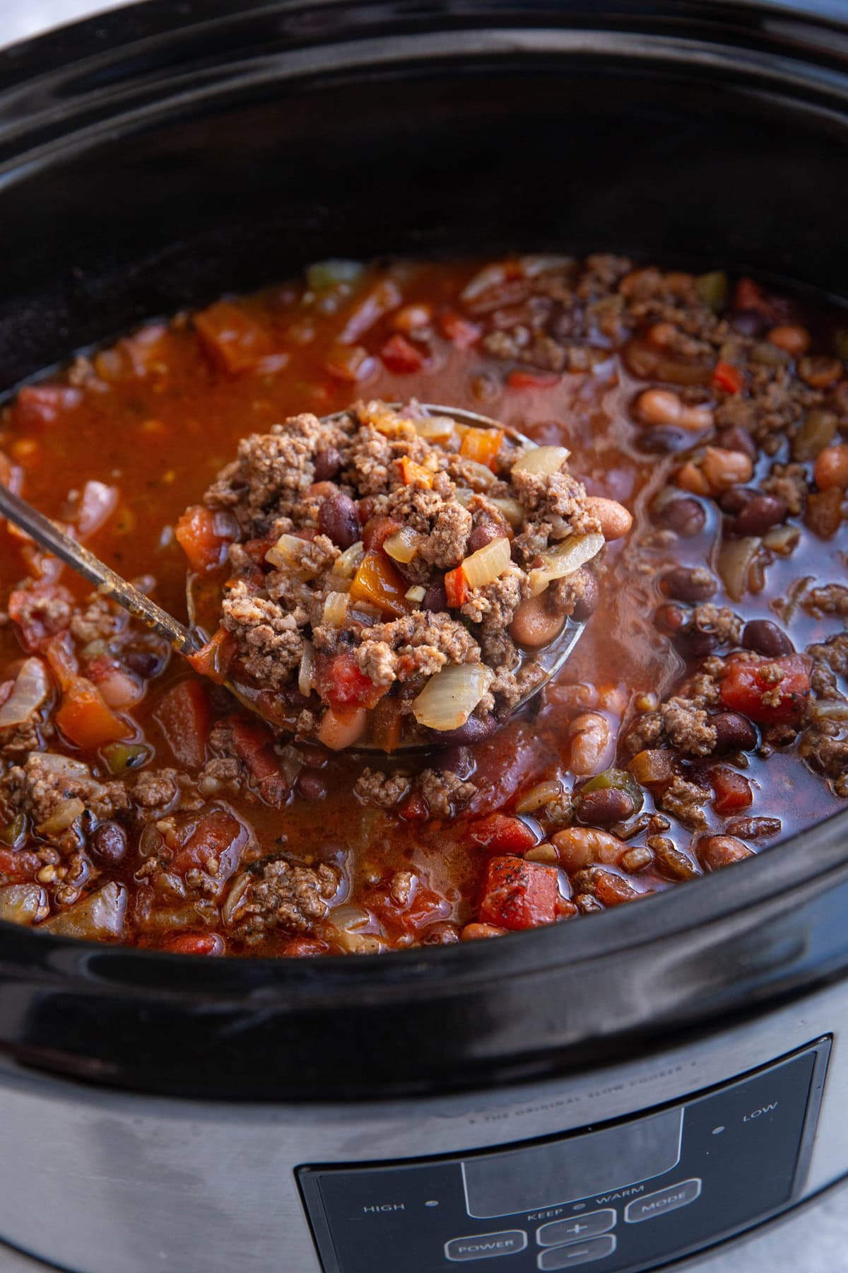 Crock pot full of chili with a ladle scooping some out.