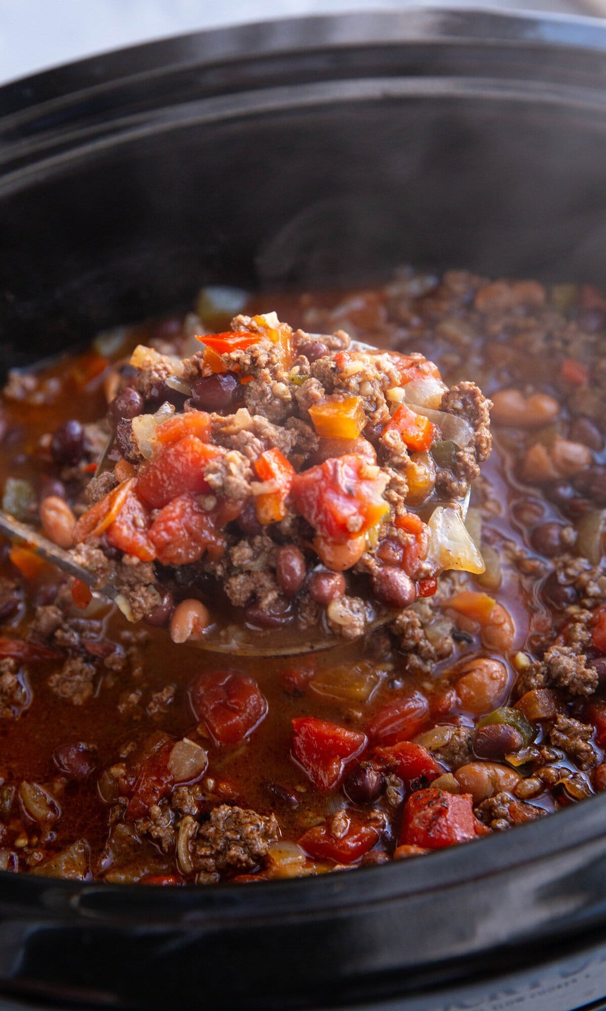 Slow Cooker full of beef chili with a scoop being taken out.