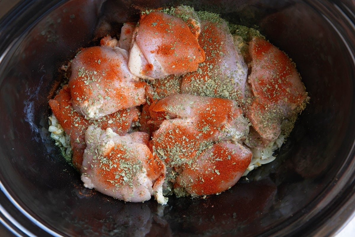 Crock pot full of chicken seasoned with paprika and oregano.