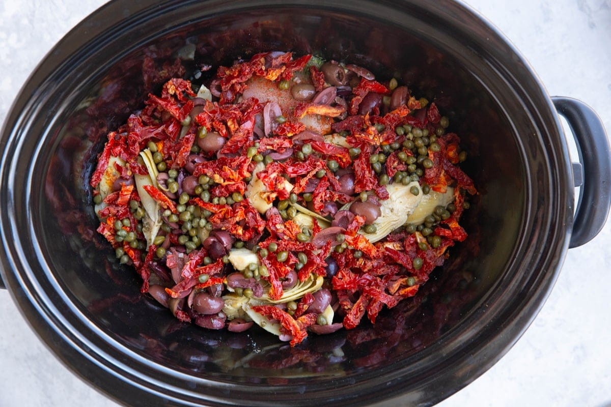 Crock pot full of chicken, sun-dried tomatoes, artichoke hearts, and kalamata olives.