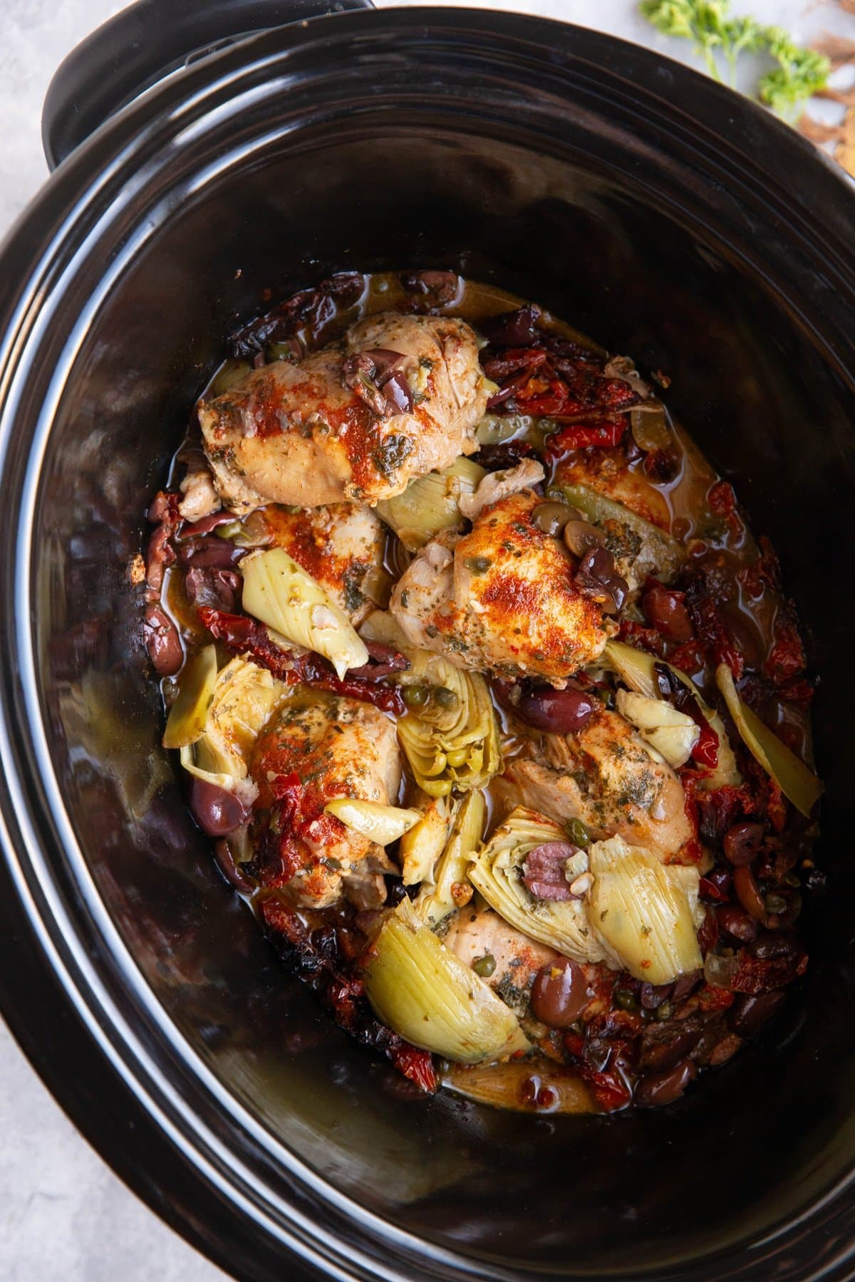 Slow cooker full of Mediterranean ingredients for a chicken dinner.