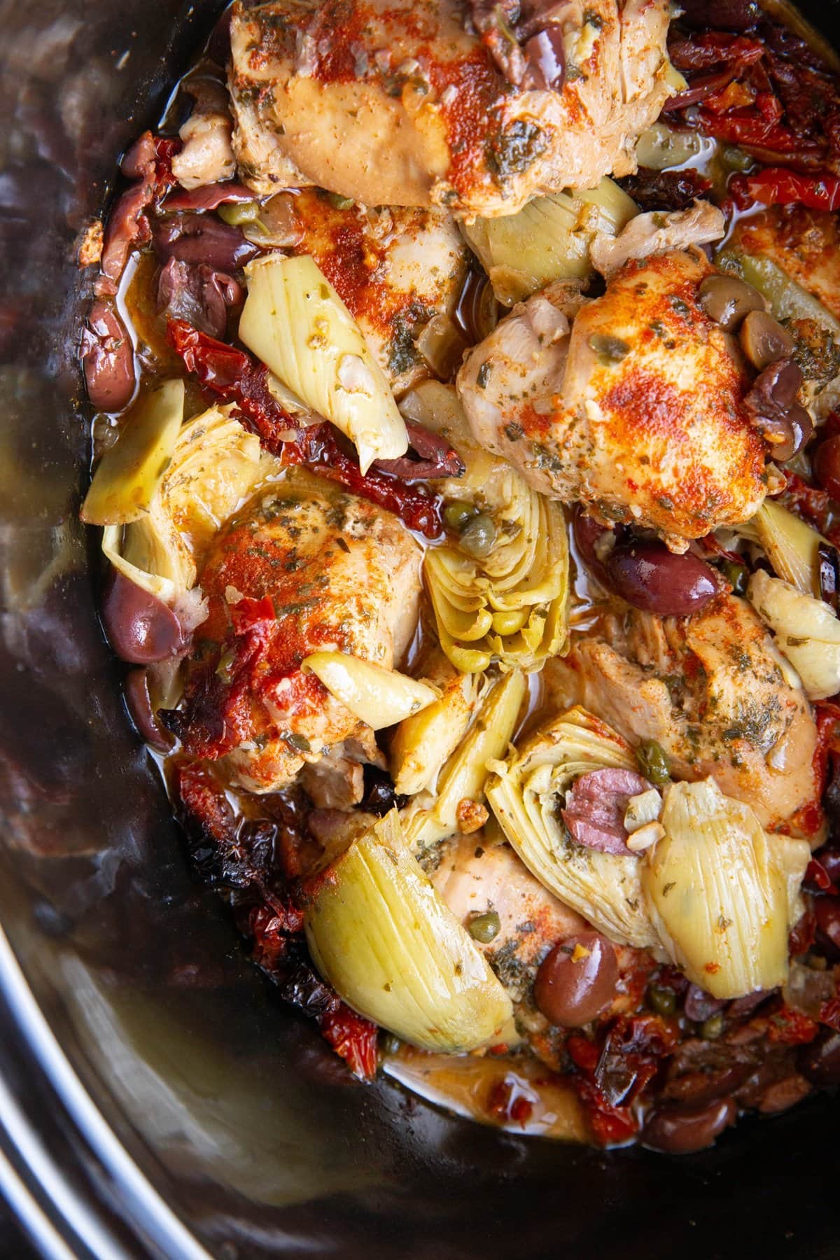 Crock pot full of chicken and Mediterranean ingredients.