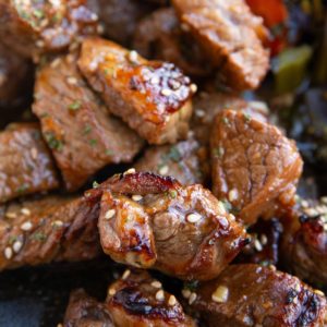 Pile of garlic steak bites on a plate with vegetables.