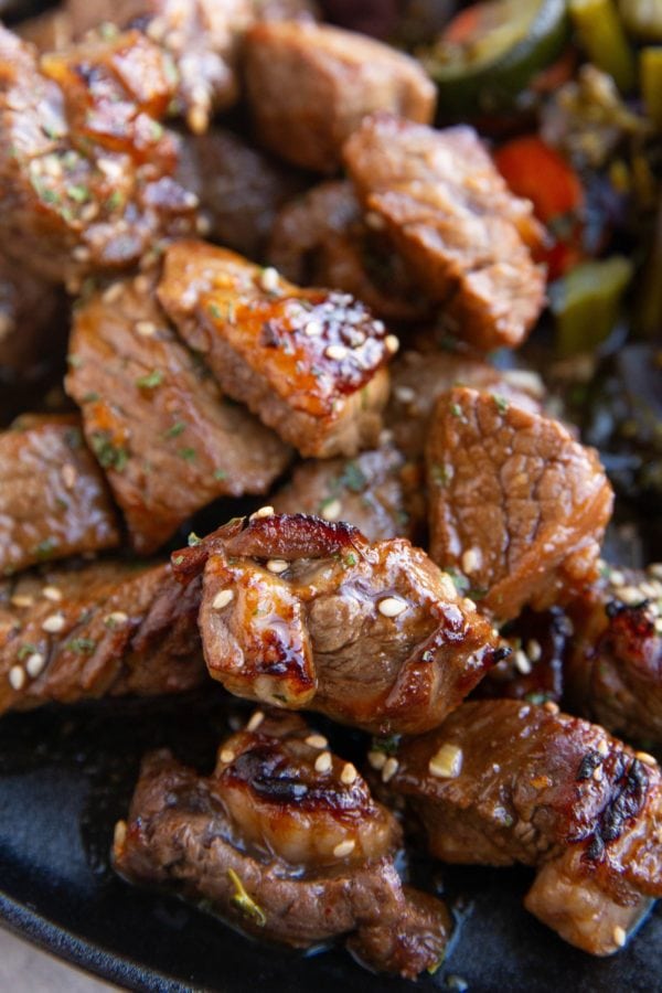 Pile of garlic steak bites on a plate with vegetables.