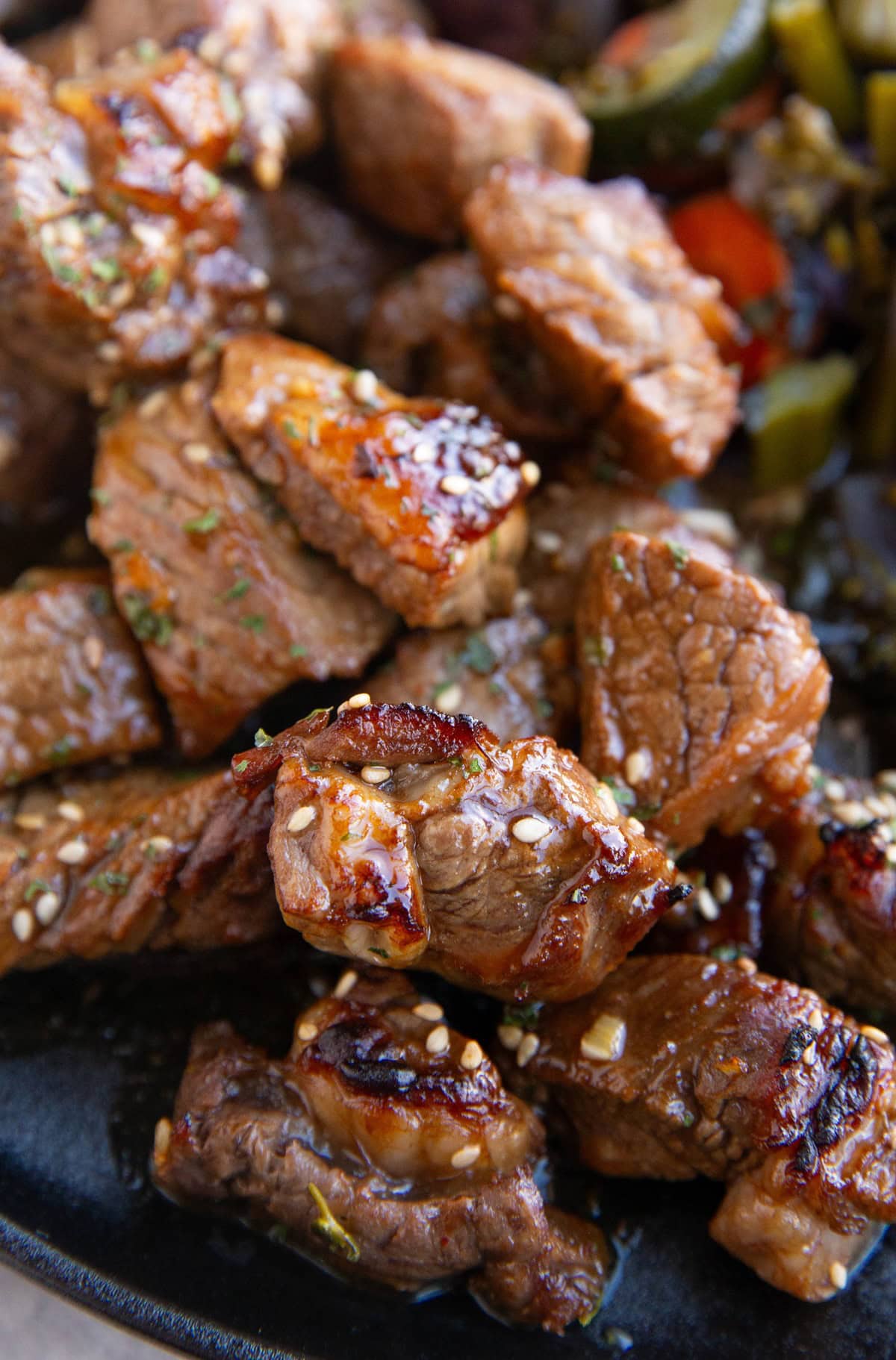 Pile of garlic steak bites on a plate with vegetables.