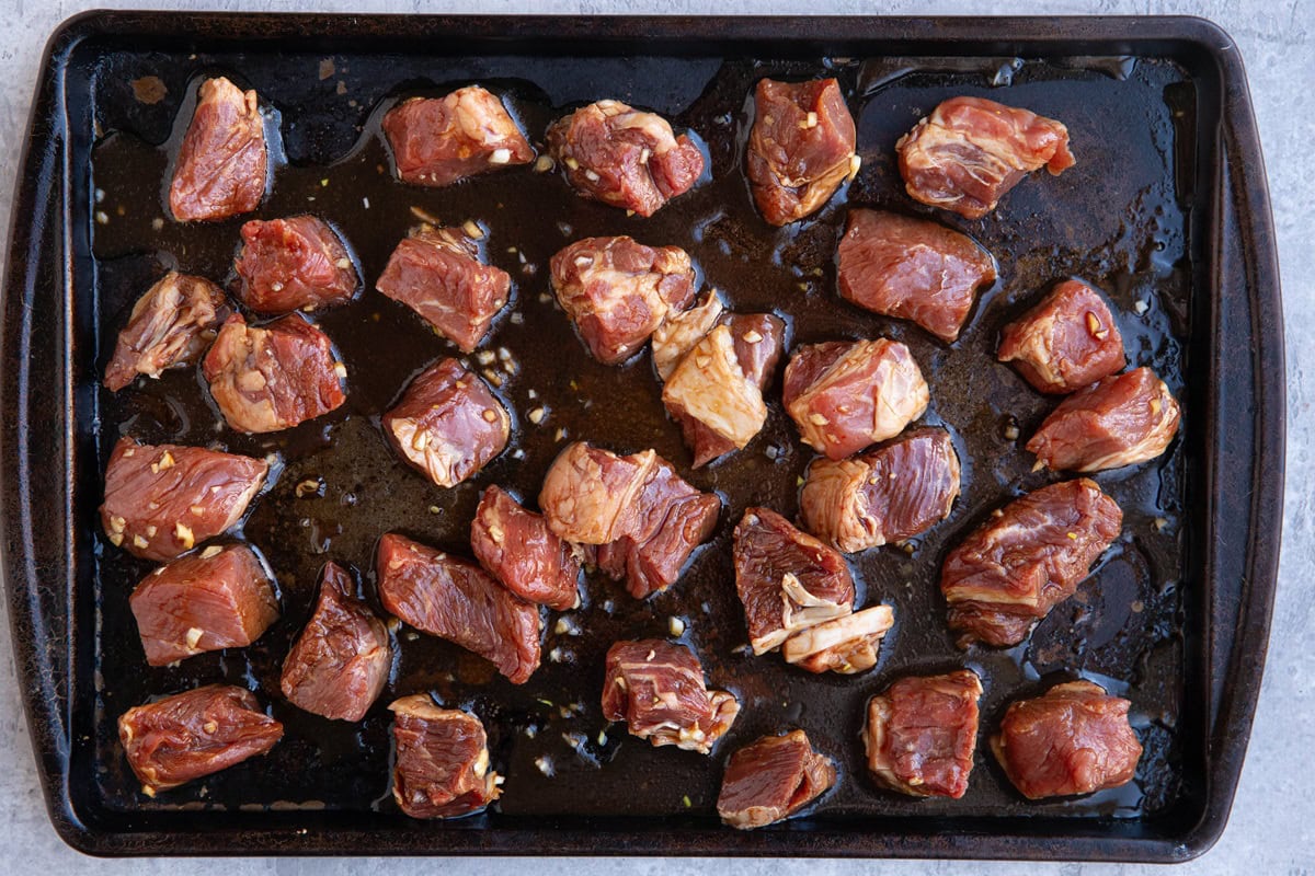 Large baking sheet with raw chunks of steak spread in a single layer.