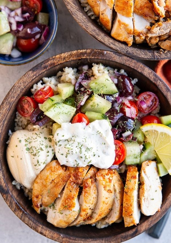 Two wooden bowls of Greek chicken bowls.