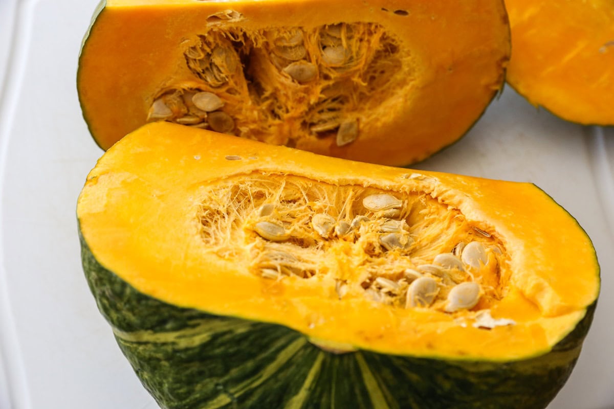 Kabocha squash cut in half, exposing the seeds and stringy insides.