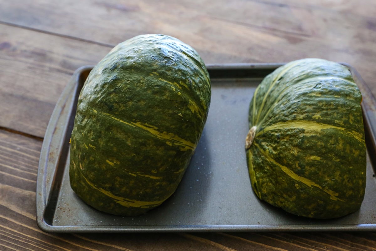 Two kabocha squash halves sitting on a baking sheet, cut side down.