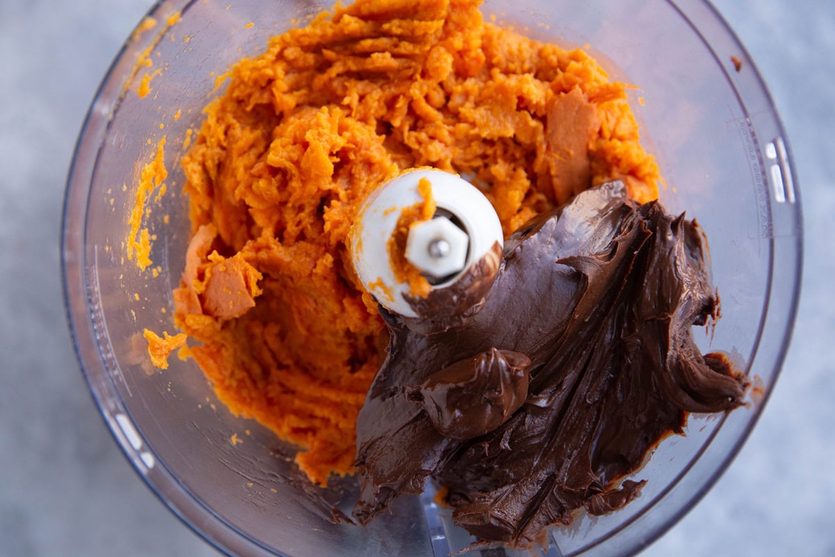 Food processor full of mashed sweet potato and melted chocolate to be blended into frosting.