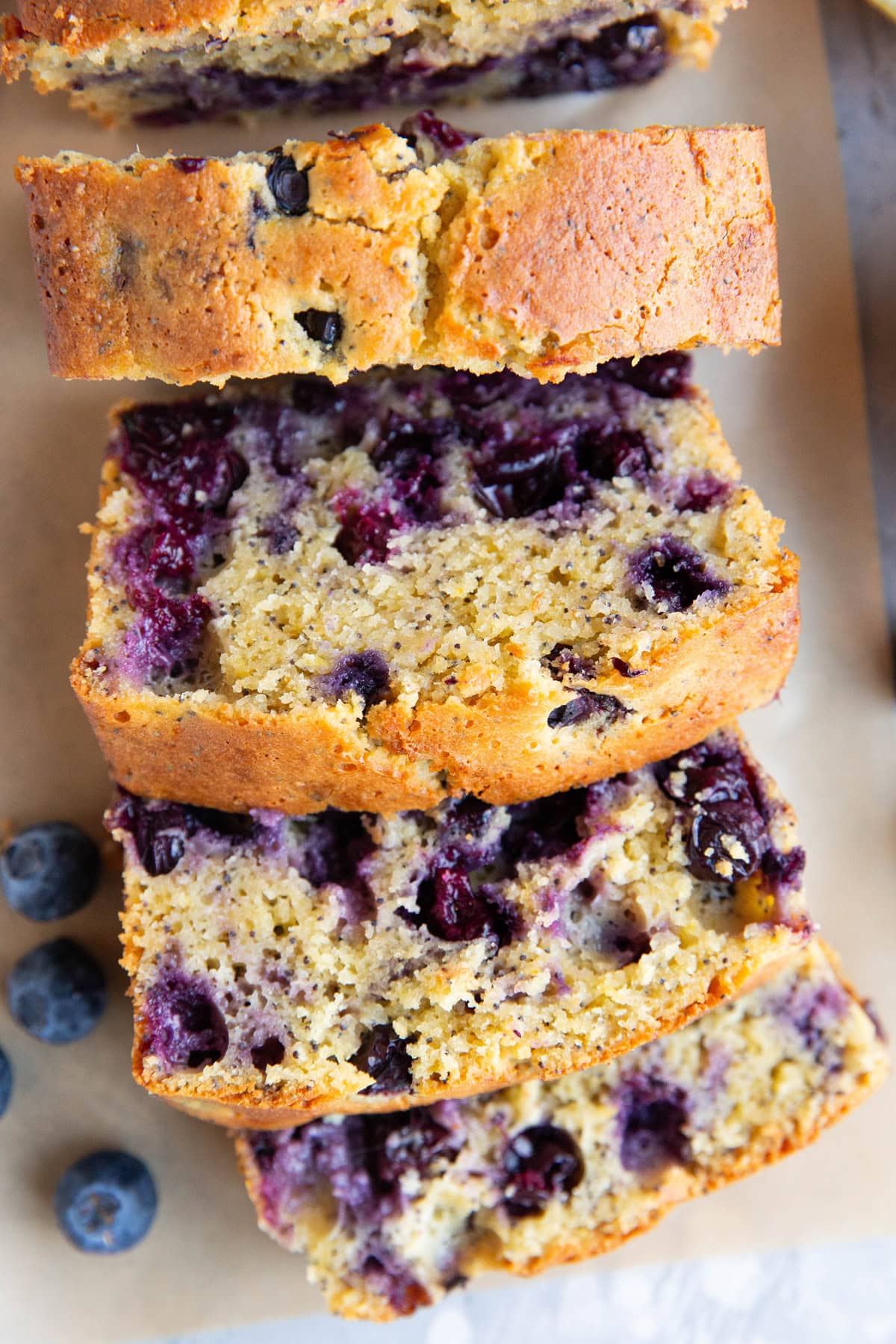 Lemon poppy seed blueberry bread cut into slices on a sheet of parchment paper.