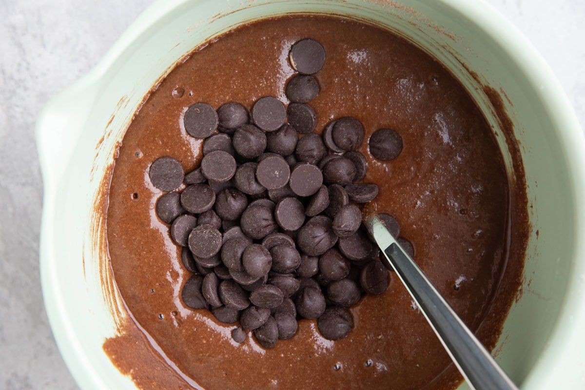 Mixing bowl full of chocolate batter with chocolate chips on top, ready to be mixed in.