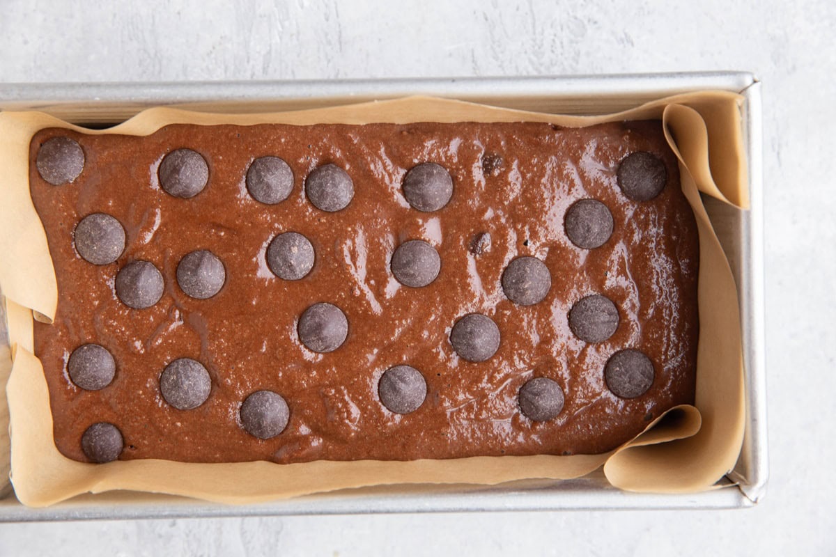 Loaf pan with chocolate batter inside, topped with chocolate chips and ready to bake.