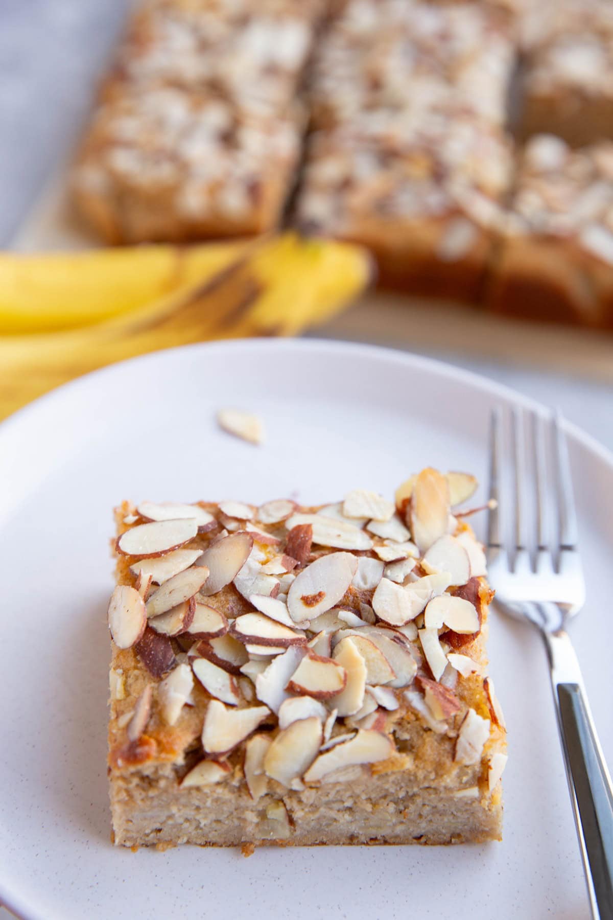 Slice of banana cake on a plate with a fork to the side.