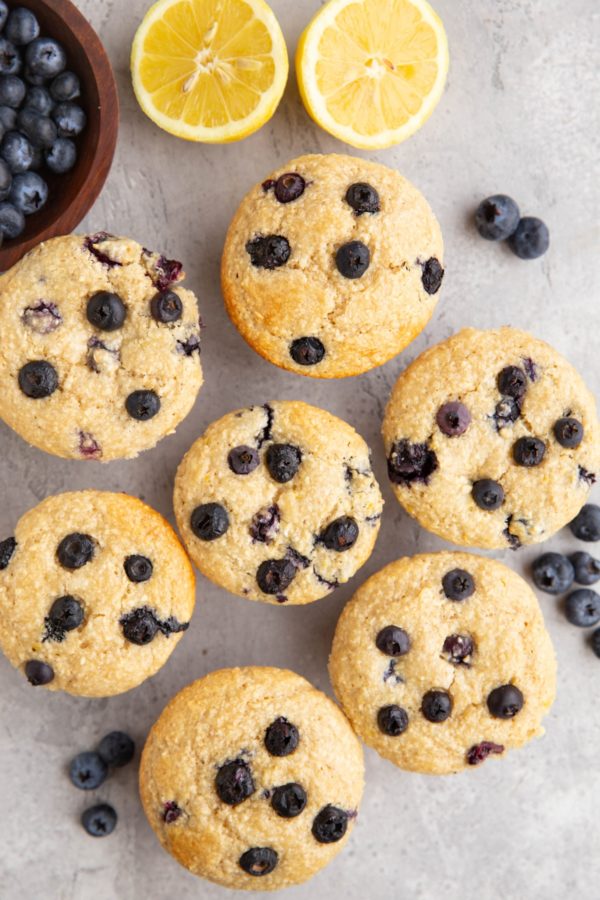 Muffins on a backdrop with blueberries all around and a fresh lemon sliced in half.