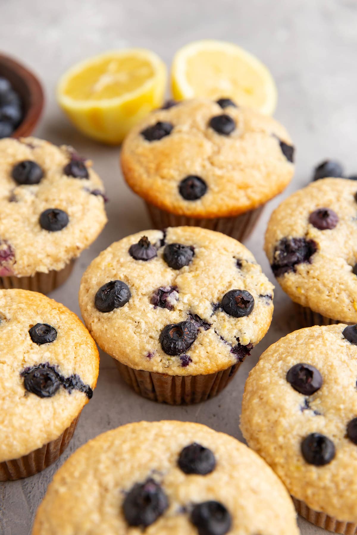 Blueberry muffins on a backdrop with fresh blueberries and a lemon in the background.