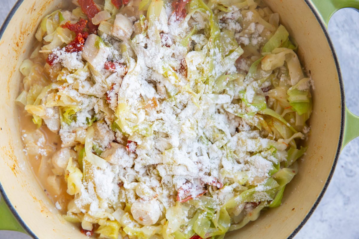 Large pot of cabbage, chicken and creamy sun-dried tomato sauce with flour sprinkled on top.