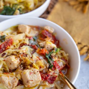 Two white bowls full of cabbage, chicken and creamy sun-dried tomato sauce.