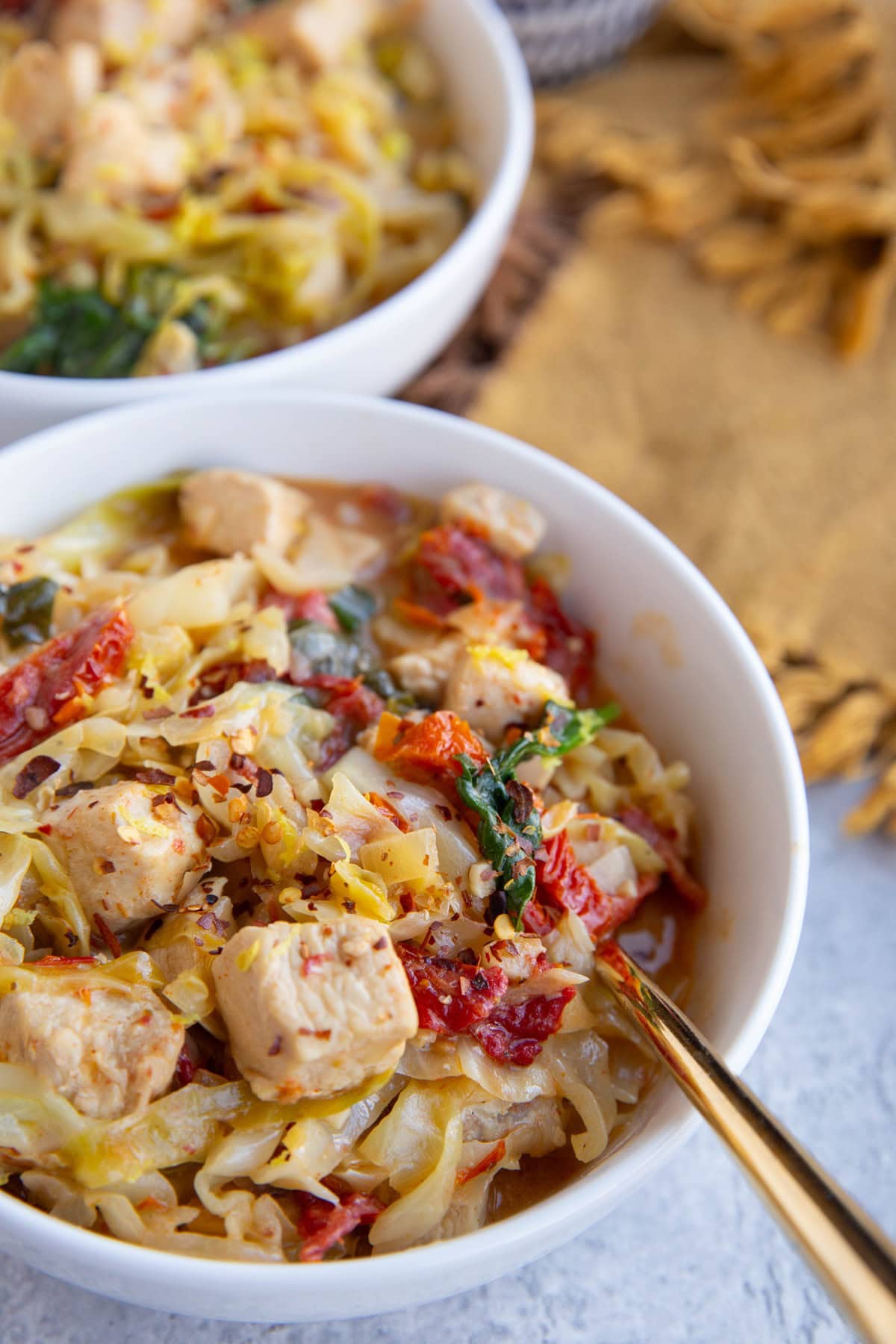 Two white bowls full of cabbage, chicken and creamy sun-dried tomato sauce.