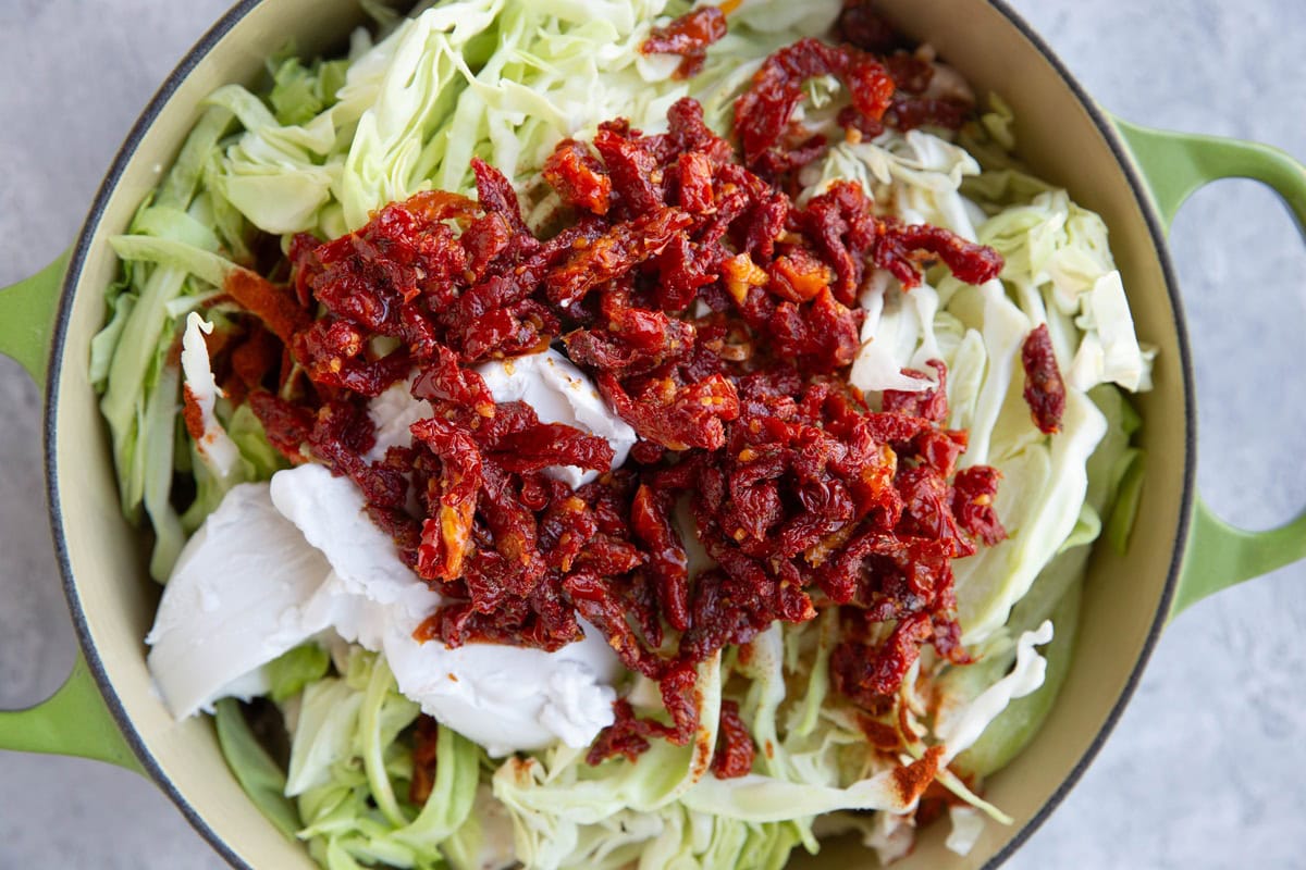 large pot full of cabbage, sun-dried tomatoes, and coconut milk.