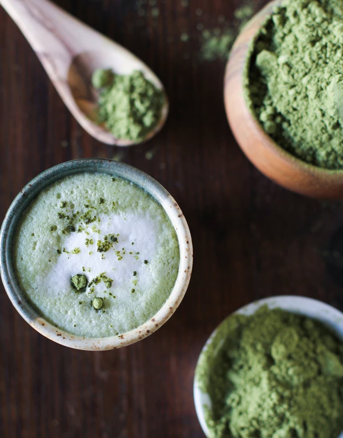 Matcha latte in a mug with a spoon and a bowl of matcha powder next to the mug. Ready to drink