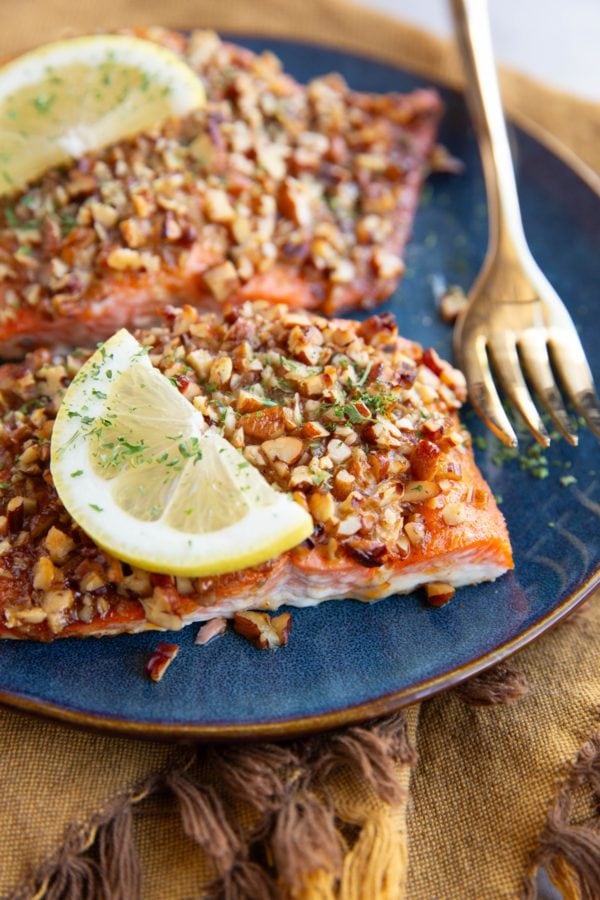 Pecan encrusted salmon filets on a plate with a golden fork and slices of lemon, ready to serve.