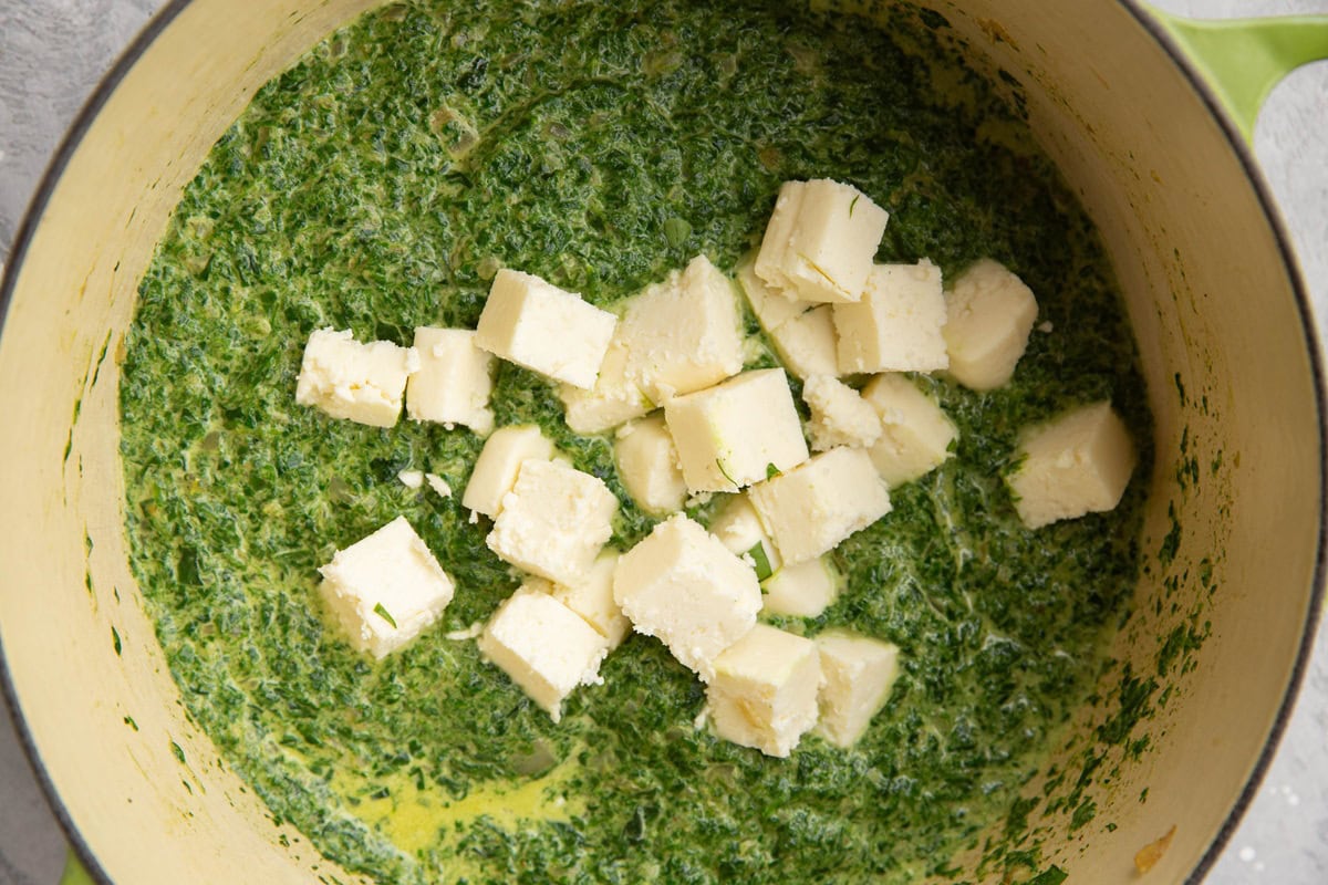 Large pot of spinach sauce with chunks of paneer added in, ready to be stirred.