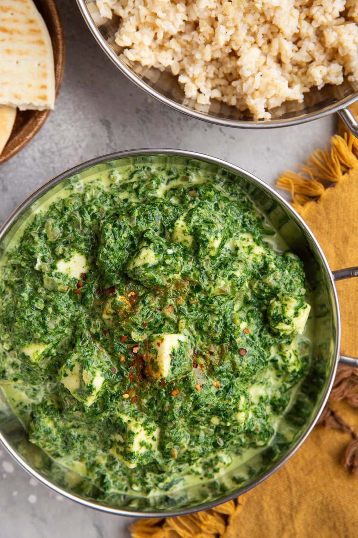 Saag paneer in a traditional Indian dish with a dish full of rice and naan to the side.