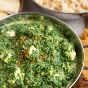 Indian dish full of saag paneer with a dish of brown rice in the background.