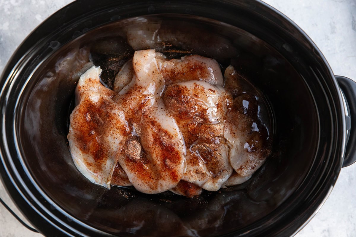 Slow cooker full of chicken breasts with spices and oil.