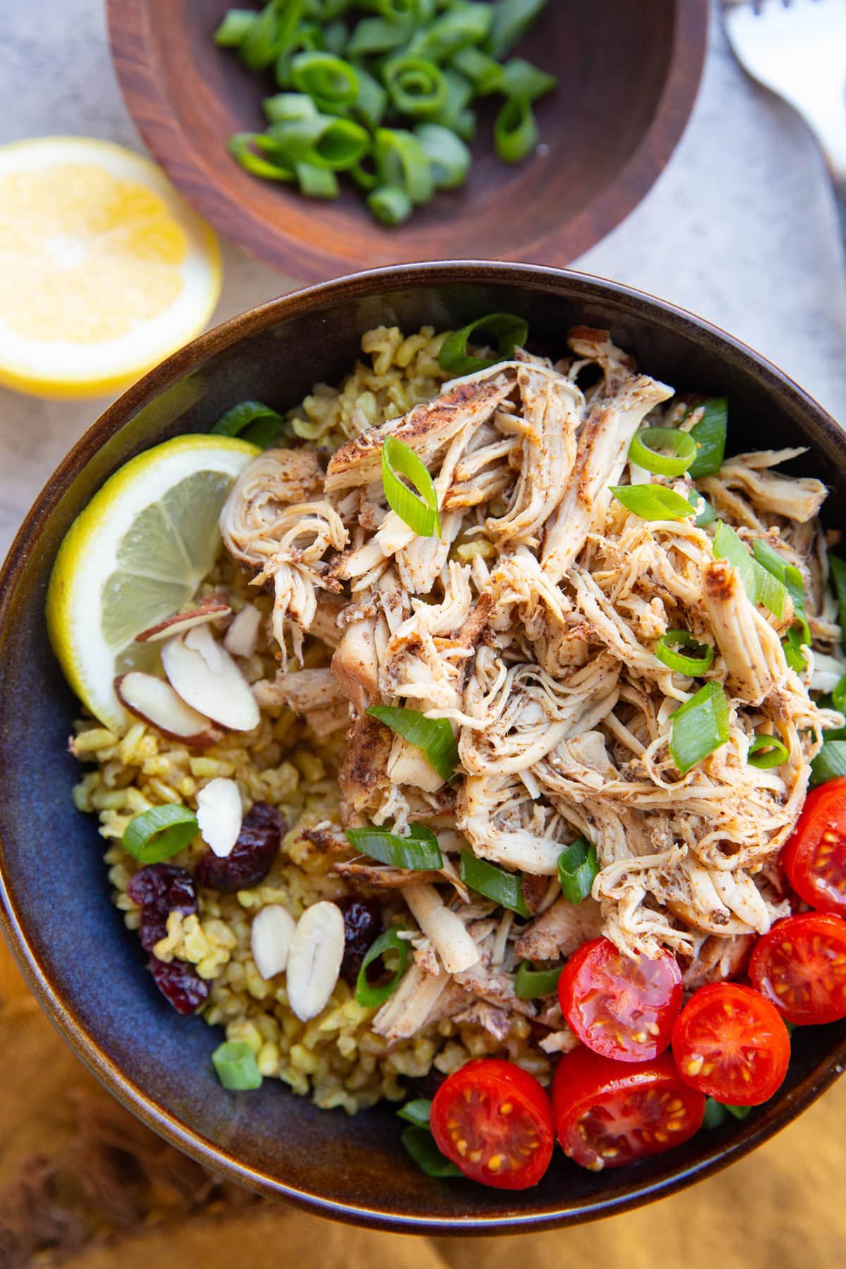 Shredded chicken in a bowl with rice, tomatoes, onions, and lemon.