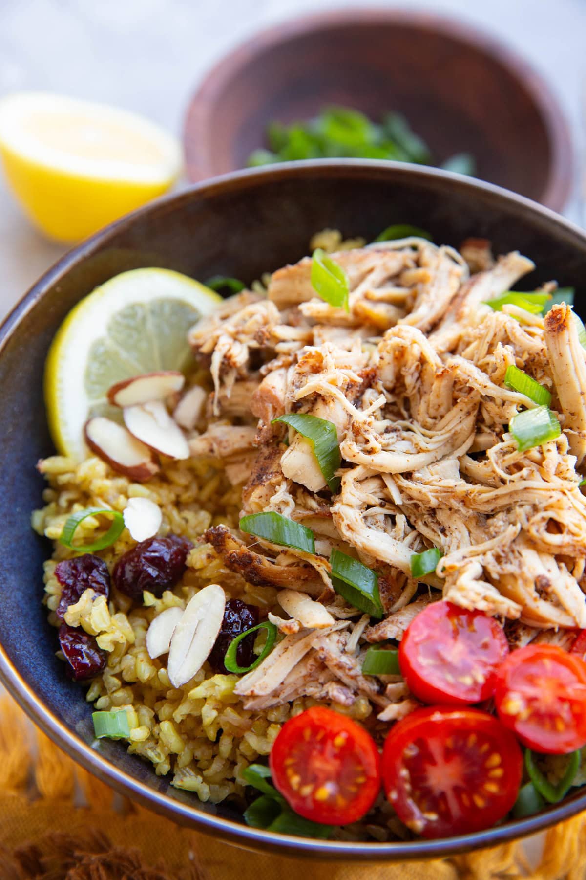 Bowl full of yellow rice and shredded chicken with chopped tomatoes, green onions and a slice of lemon.