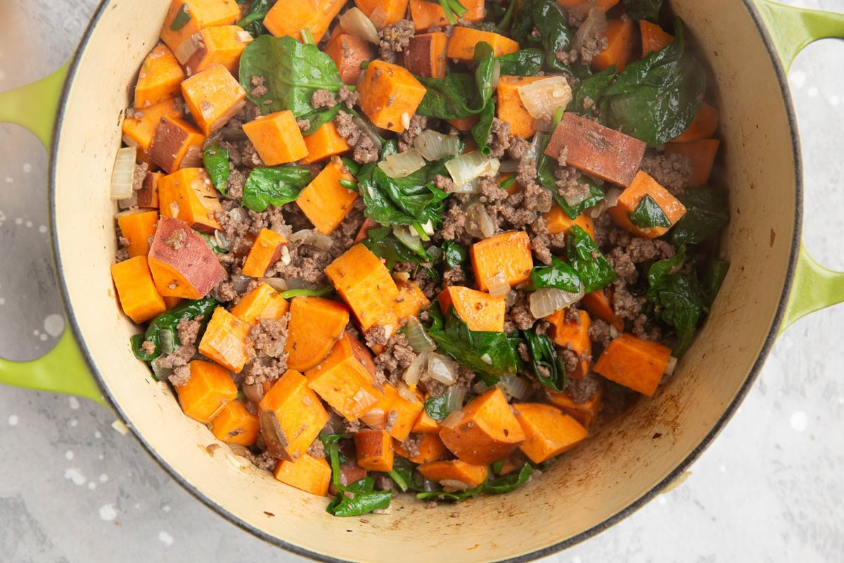 Spinach, sweet potatoes, ground beef, and onion cooking in a large pot