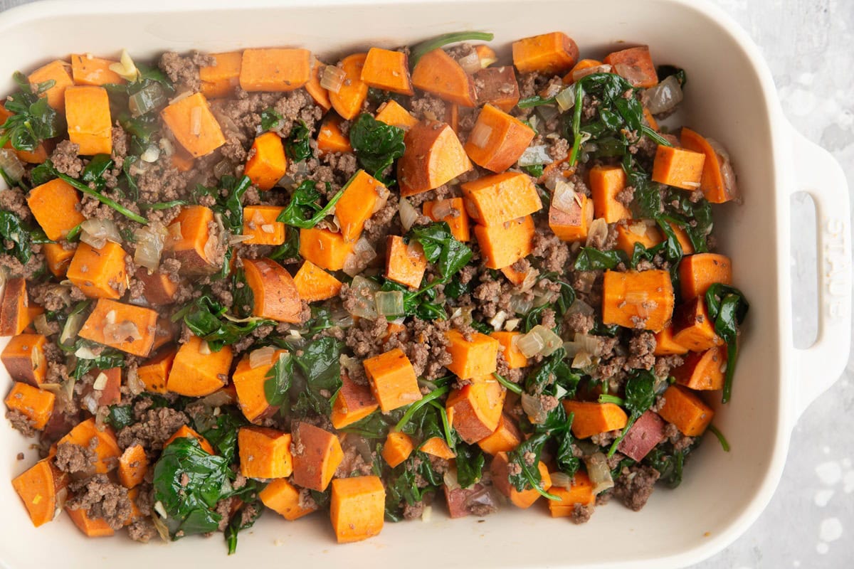 Casserole dish full of sweet potatoes, ground beef, and spinach.