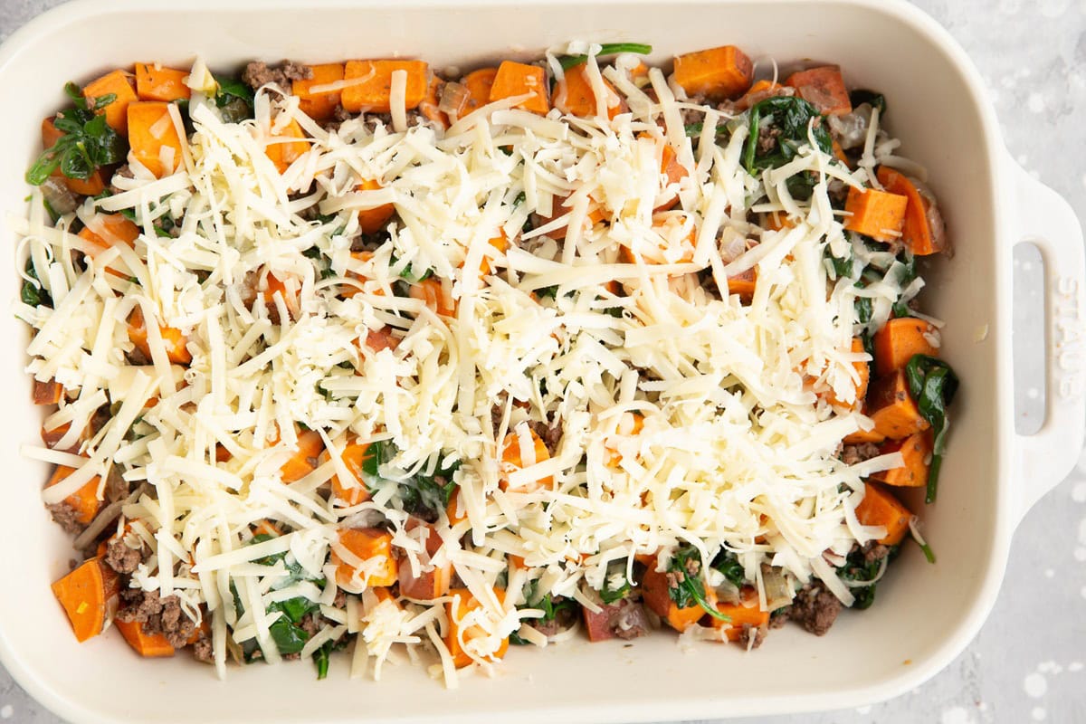 Large casserole dish full of beef, sweet potatoes, and spinach sprinkled with cheese.