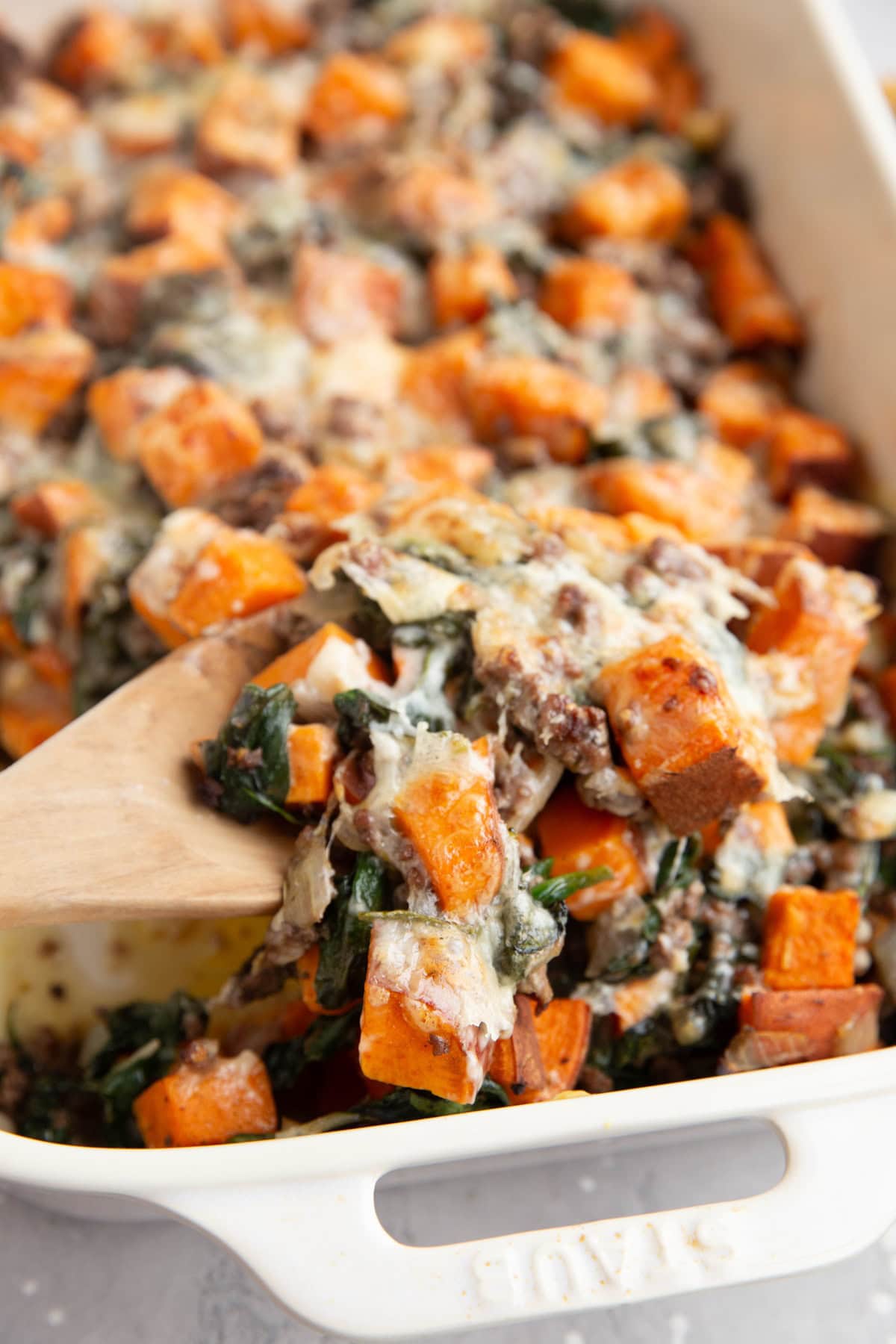 Ground beef and sweet potato casserole with a wooden spoon scooping some of it out to serve.