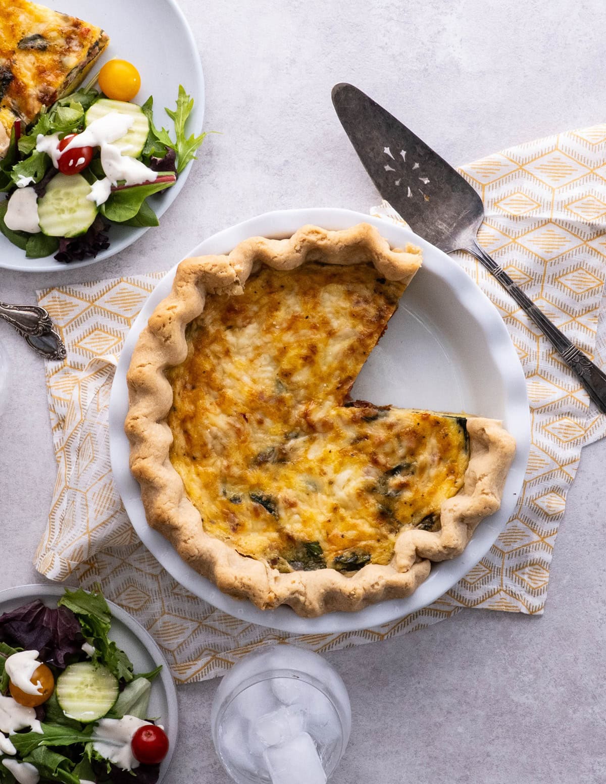 Quiche on a table with a slice taken out and a plate of salad.